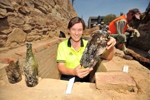 Archaeologist standing in a trench holding a bottle.